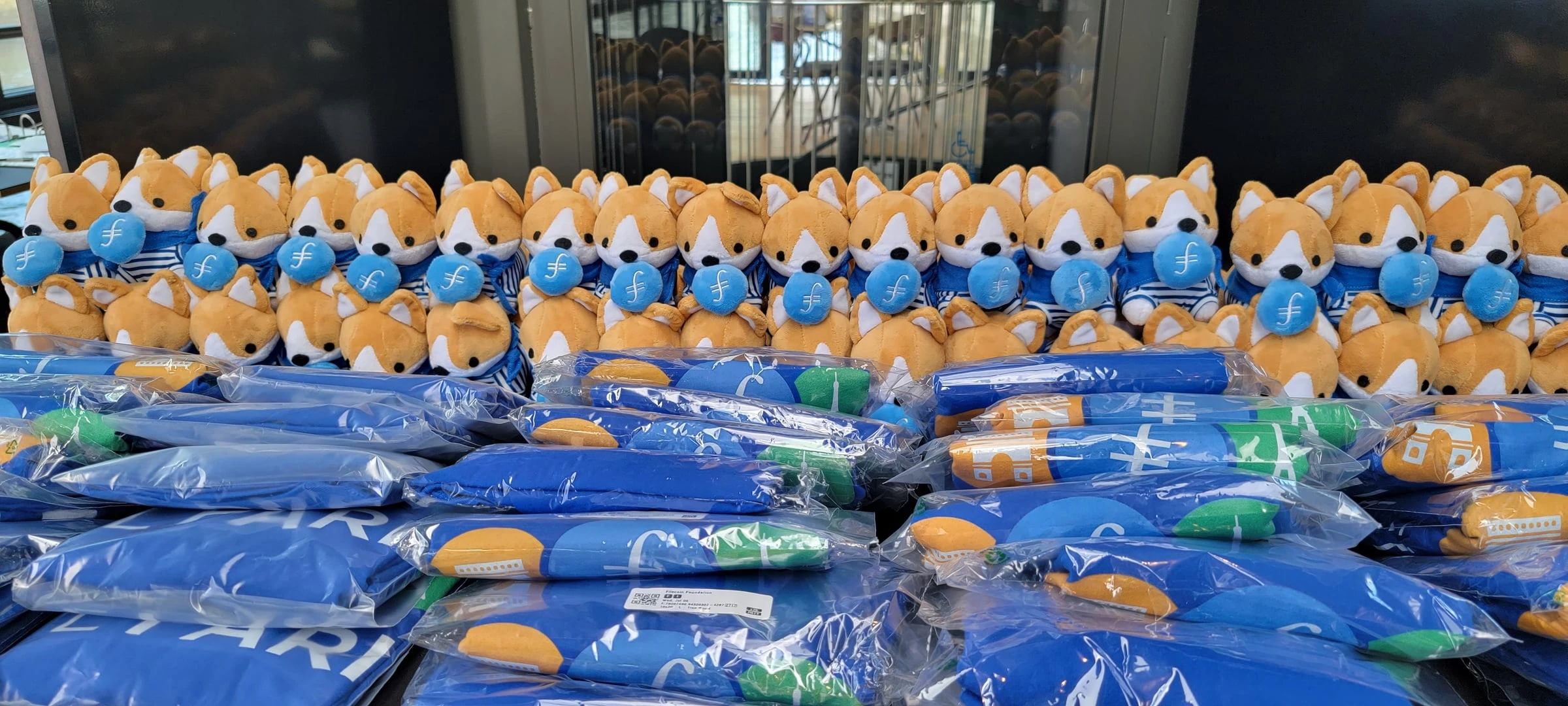Rows of Filecoin corgi plushies and blue tote bags laid out ready for FIL Paris