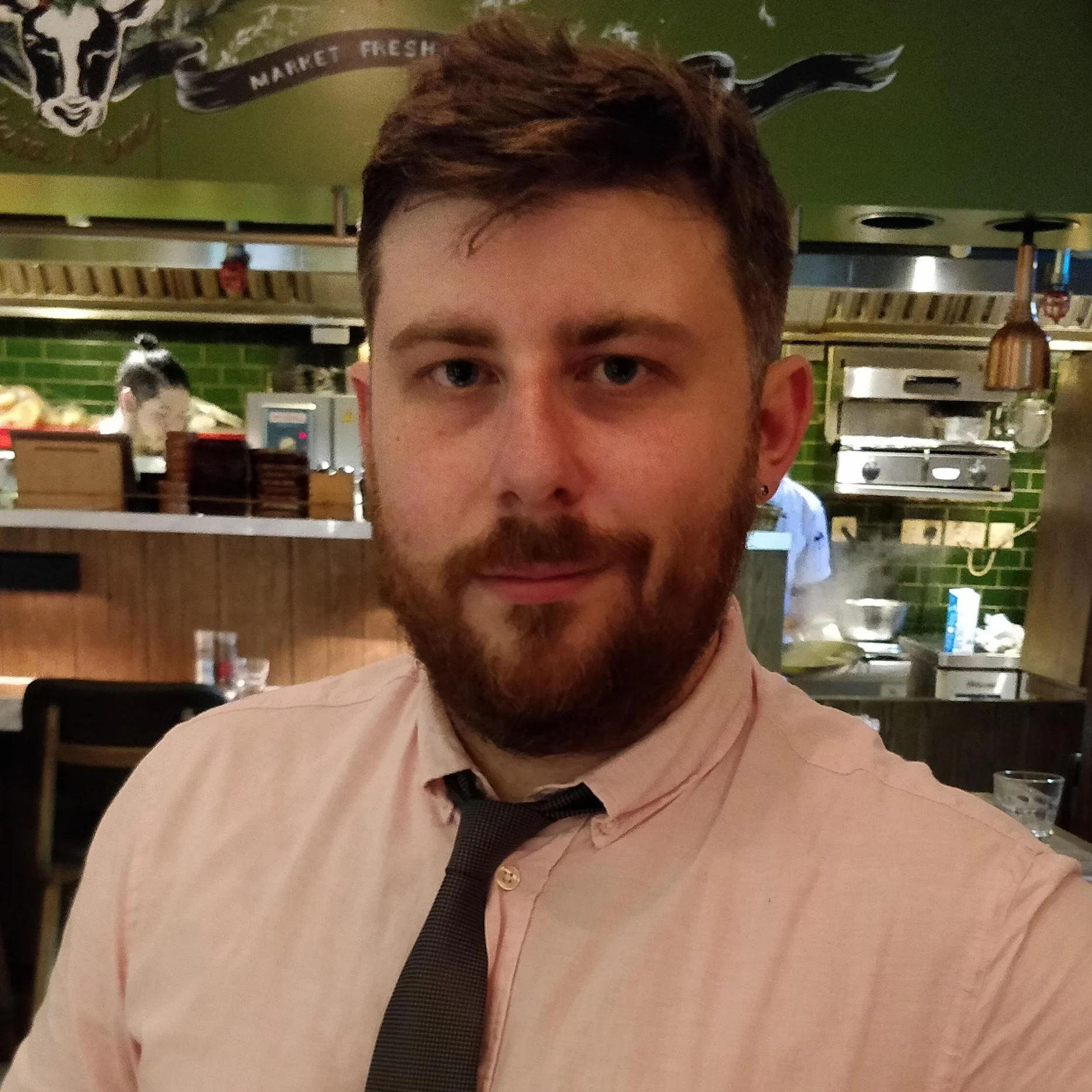 Gary Moran in a pink shirt and tie at a restaurant counter, the open kitchen behind him