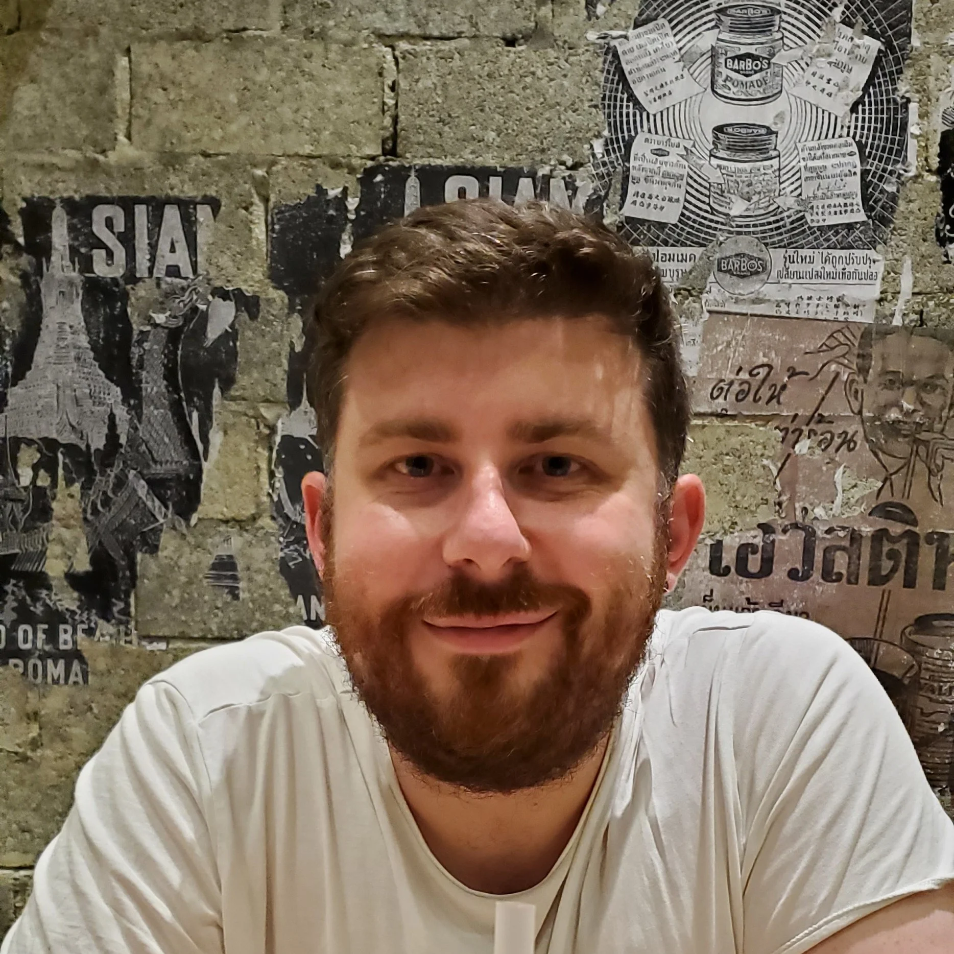 Gary Moran at a table with a mango drink, a poster-covered brick wall behind him